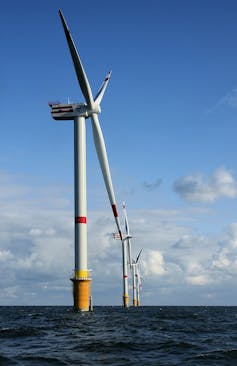 A wind turbine with three thin blades rising out of the water.